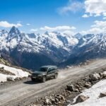 SUV driving on a high altitude mountain pass road with snow patches and dramatic peaks
