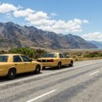 Two identical sedan taxis parked side by side on a highway shoulder with mountains in the distance