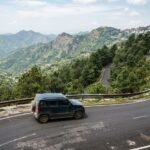 SUV taxi driving on a winding hill road climbing toward Mussoorie with pine trees and valley views