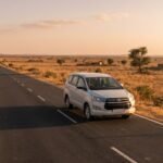 Innova Crysta taxi on a long open highway across dry Rajasthan plains at golden hour