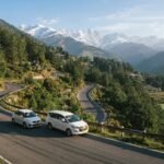 Sedan and Innova Crysta taxi driving on a winding Himachal hill road lined with pine trees